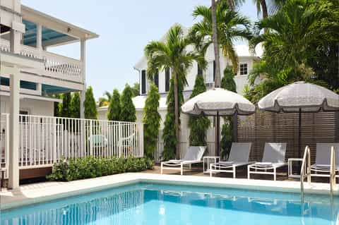 Residential pool area with white deck chairs, thatched umbrellas, white railings, and palm trees
