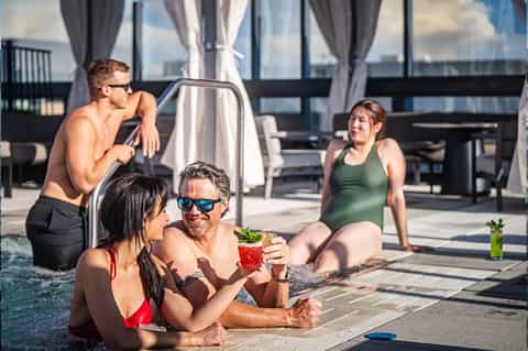 Group of guests socializing in shallow pool area with city skyline views at rooftop