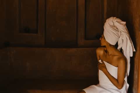Woman in spa with white towel wrap and turban in dark wooden sauna or steam room