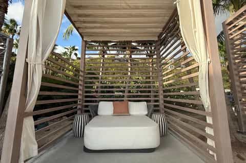 Wooden bed canopy with slatted sides and flowing white curtains on outdoor patio