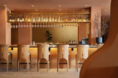 Elegant bar counter with wood paneling, hanging glassware, and bottles displayed on illuminated upper shelf