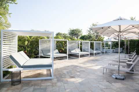 Luxury resort patio with lounge beds, pergola, umbrellas, and lush landscaping