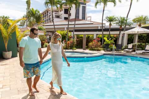 Couple walking by a curved resort pool with palm trees and modern architecture