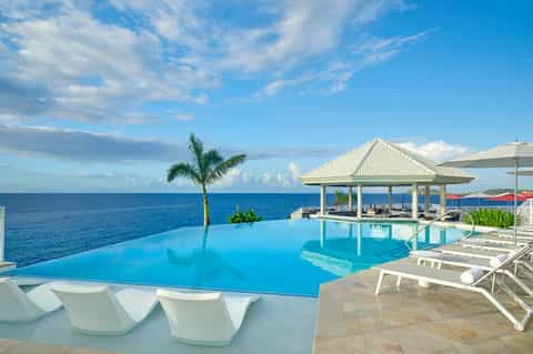 Infinity pool overlooking the ocean with white lounge chairs and a gazebo pavilion