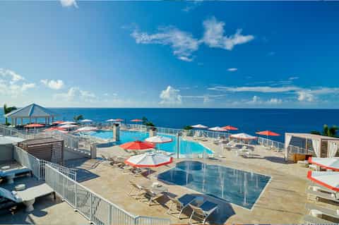 Oceanfront pool deck with red umbrellas overlooking turquoise ocean and white railings