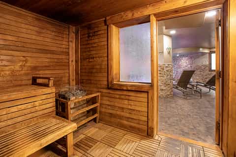 Wooden sauna interior with wooden benches, window, and adjoining spa relaxation room with loungers