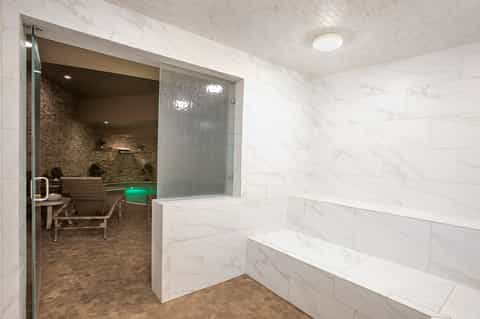 Luxury spa sauna entrance with frosted glass door and marble tiled walls with bench seating