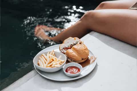 Person enjoying burger and fries by a resort pool with sparkling water