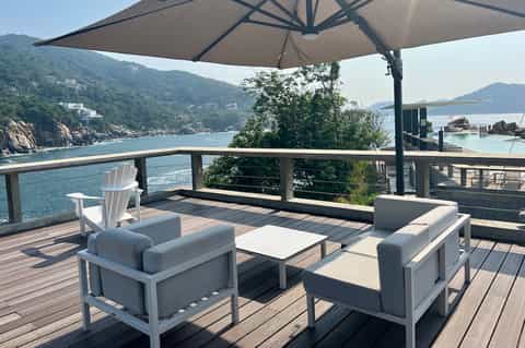 Waterfront deck with modern furniture and umbrella overlooking scenic bay with forested cliffs