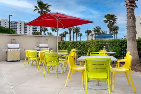 Outdoor patio with bright yellow chairs, red umbrella, grills, and palm trees overlooking a coastal landscape