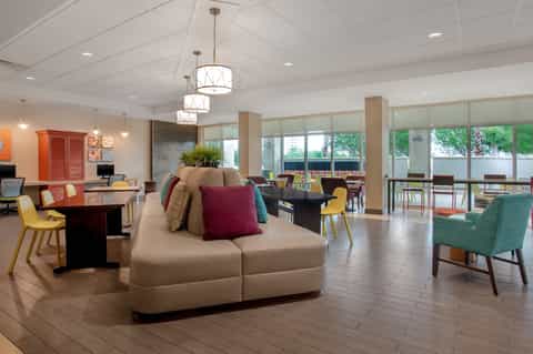 Spacious hotel lobby lounge with colorful accent seating, modern pendant lights, and floor-to-ceiling windows