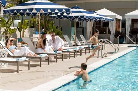 Hotel pool area with guests relaxing under navy and white striped umbrellas and lounge chairs