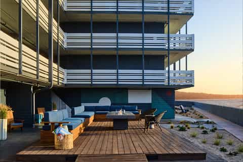 Modern beachfront deck with multi-level balconies, blue seating, and fire pit at sunset