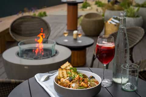 Contemporary outdoor dining setup with fire pit, wine, and seafood pasta dish at dusk