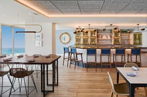 Modern beachfront restaurant with ocean views, wooden tables, and a sophisticated bar area