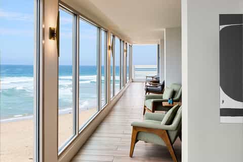 Oceanfront balcony with floor-to-ceiling windows overlooking beach and waves