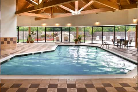 Indoor heated swimming pool with wooden beam ceiling, large windows overlooking outdoor deck area