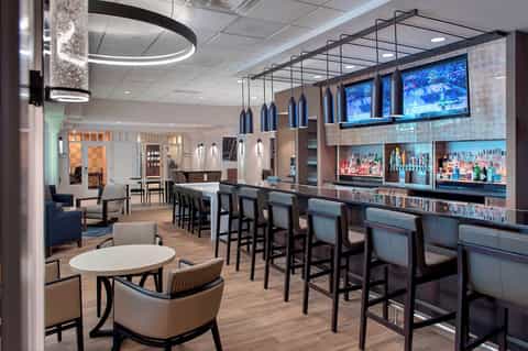 Contemporary hotel bar and lounge with blue pendant lights, full bar, and seating area