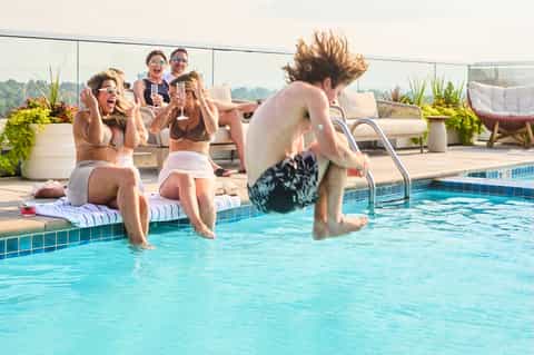 Group of young adults enjoying rooftop pool party with high-rise city views and poolside seating