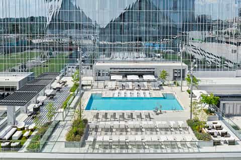Aerial view of resort pool deck with loungers, landscaping, and surrounding buildings