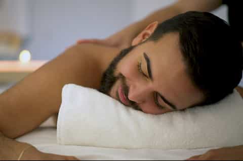 Man relaxing on white pillow with peaceful expression in spa treatment setting
