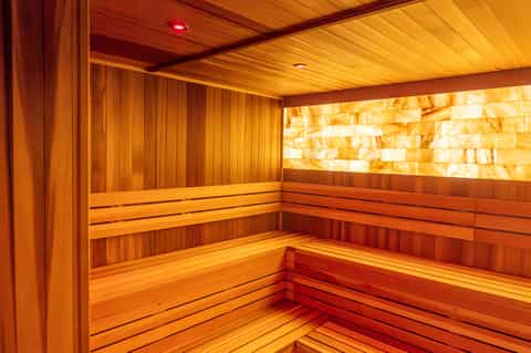 Modern sauna interior with warm wood paneling, tiered benches, and golden onyx wall lighting