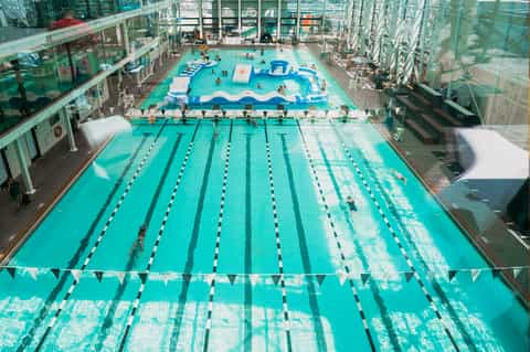 Lap pool with lane dividers indoors, featuring glass ceiling and adjoining leisure pool with guests