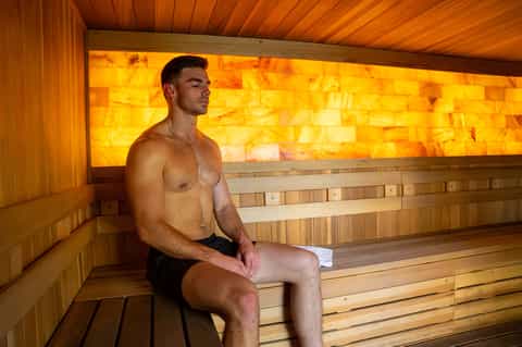 Man in sauna room with wooden walls and golden amber illuminated salt brick wall backdrop