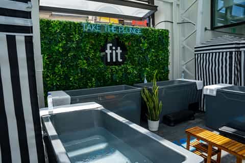 Modern rooftop lounge with green living wall, neon 'Take The Plunge' sign, and soaking tubs with seating