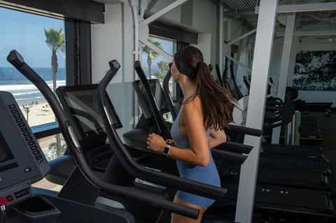 Woman exercising on elliptical machine in bright gym with ocean and beach views