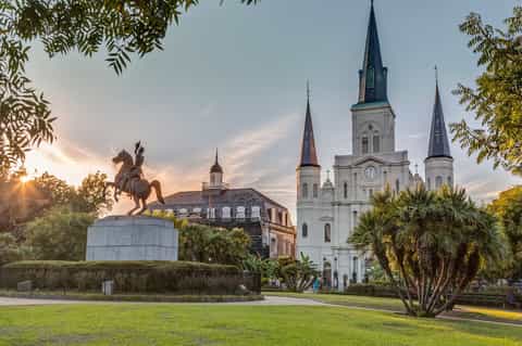 Historic white cathedral with equestrian statue at sunset, palm trees, and manicured grounds