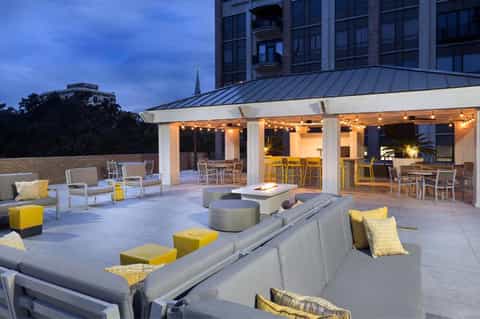 Rooftop terrace with fire pit, gray seating, yellow accents, modern pavilion, and city skyline at dusk