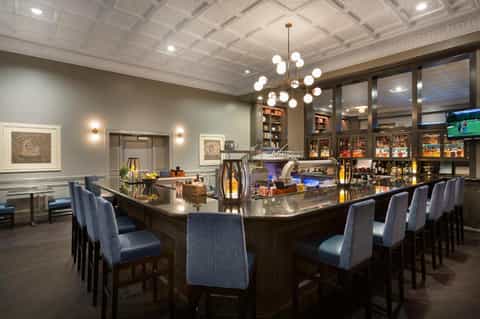 Upscale hotel bar lounge with dark wood counter, blue seating, and coffered ceiling