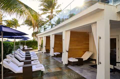 Luxury resort cabana with white lounge chairs, curtains, and palm trees overhead