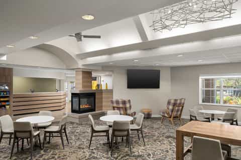Modern hotel lobby lounge with fireplace, skylight, seating areas, reception desk, and contemporary decor