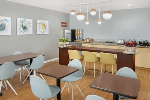 Bright break room with dining tables, yellow chairs, beverage station, and colorful wall art