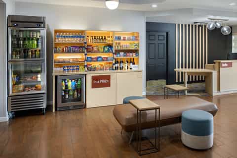 Hotel lobby and convenience store with beverage coolers, snacks, seating area, and check-in desk