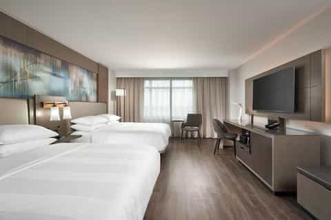 Modern hotel guest room with two queen beds, TV, desk, contemporary furnishings, and garden views
