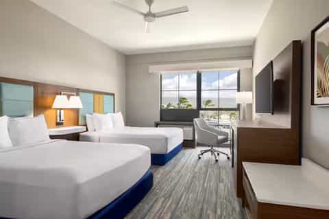 Hotel room with two queen beds, ocean view, desk area, and TV mounted on wall