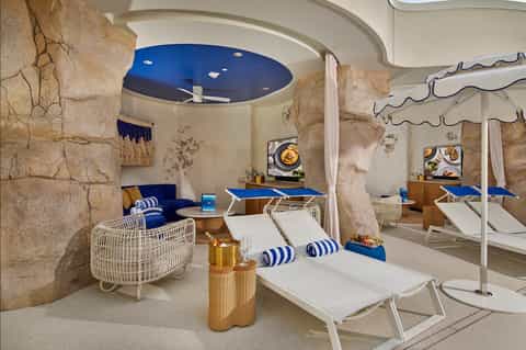 Luxury spa relaxation area with stone boulders, blue ceiling, white lounge chairs, blue accents, and modern decor