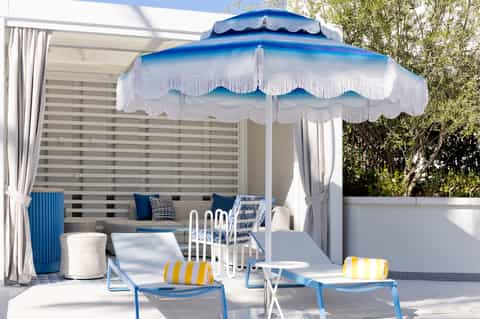 Luxury cabana with blue and white striped canopy, lounge seating, and fringe details