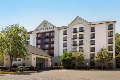 Hyatt Place hotel exterior with multi-story cream building, red roof accents, and manicured landscaping