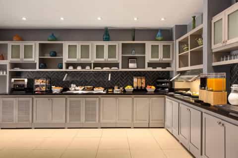 Hotel buffet breakfast area with white cabinetry, black herringbone backsplash, and beverages