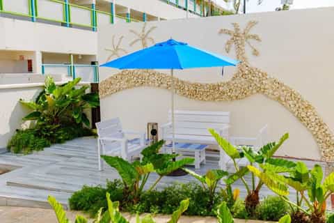 Beach-themed courtyard with seashell wall art, blue umbrella, white bench, and tropical plants