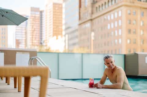 Woman in pool at rooftop urban hotel with city skyline and green barriers visible