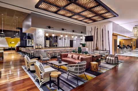 Upscale hotel lobby with bar, lounge seating, decorative pendant lights, and modern geometric ceiling design.