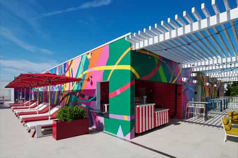 Colorful beach cabanas with vibrant geometric artwork, red umbrellas, loungers, and pergola shade