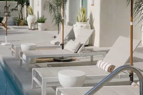 Minimalist pool deck with white loungers, potted plants, and clean Mediterranean-style courtyard