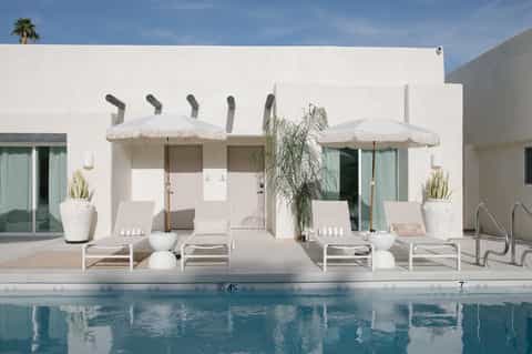 Modern poolside cabanas with white umbrellas and loungers overlooking turquoise swimming pool