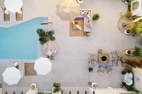 Overhead view of resort pool deck with white umbrellas, loungers, palm tree, and terrace areas